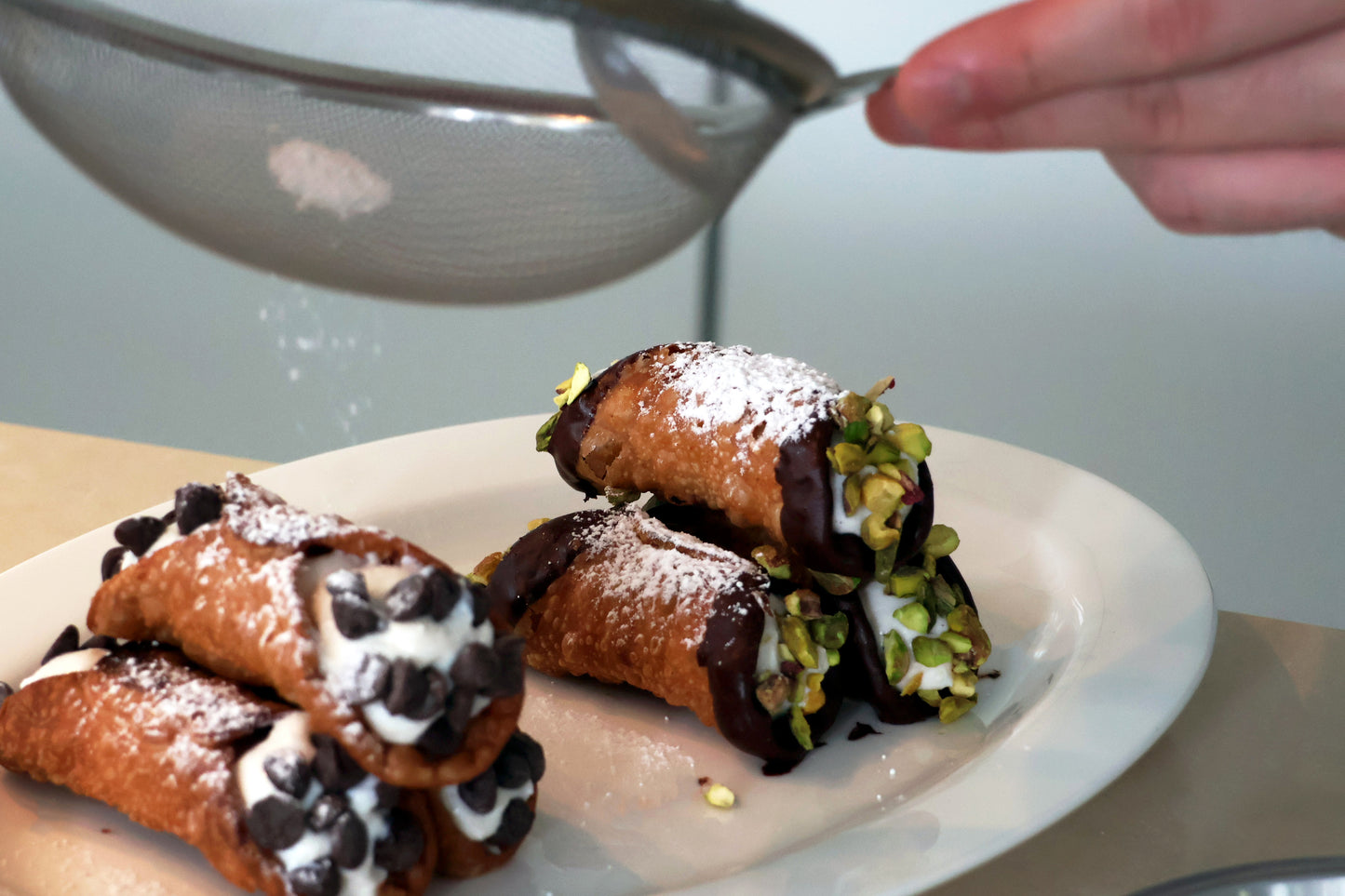 Deep fried cannoli (Chocolate and pistachio flavoured ones) being dusted with icing sugar.