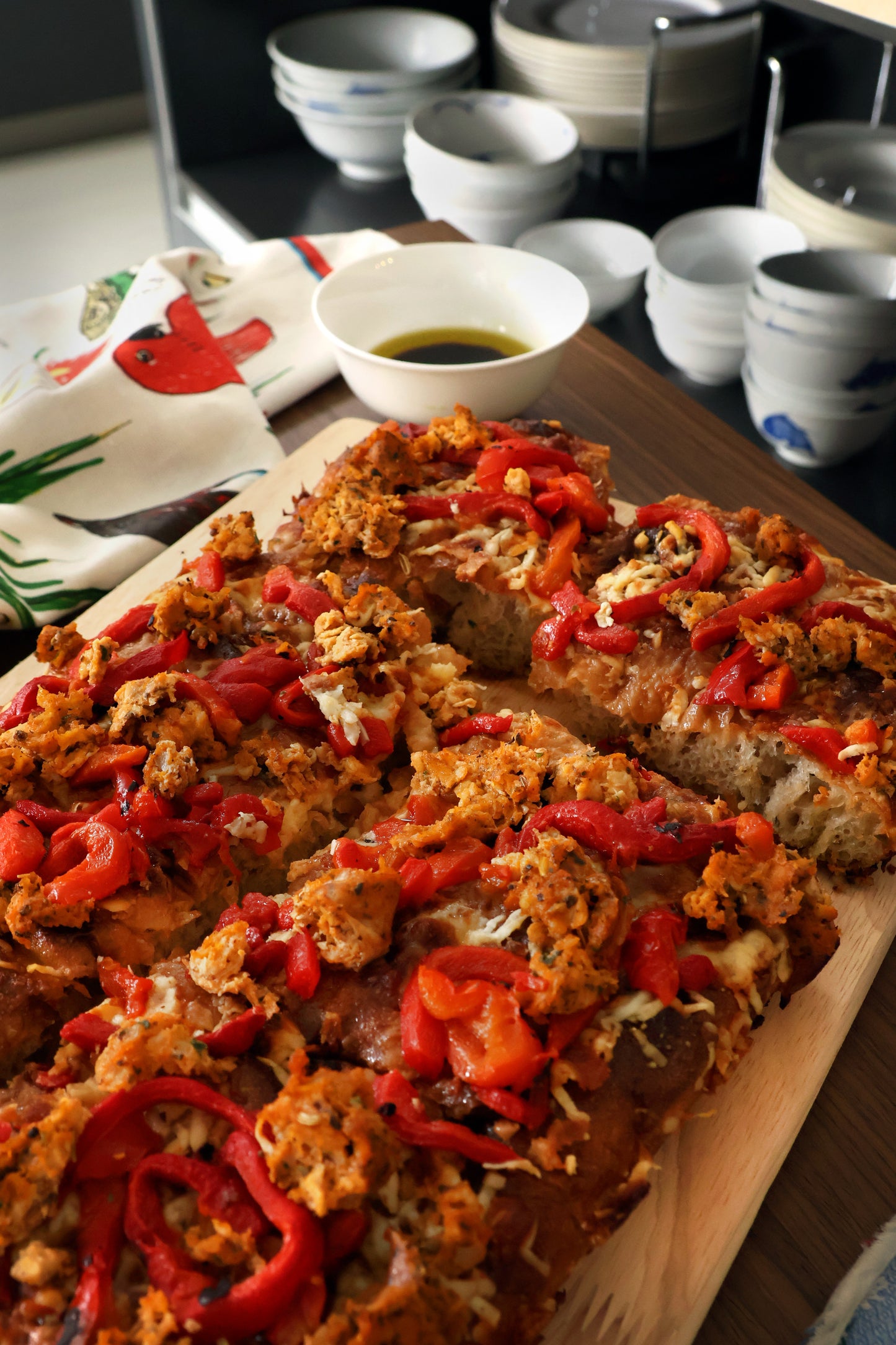 Detroit pizza topped with a mixture of ingredients. The toppings include shredded chicken sausages, red bell peppers, and cheddar cheese, creating a colorful and appetizing presentation. Overall look is inviting, indicating a flavorful and hearty meal.