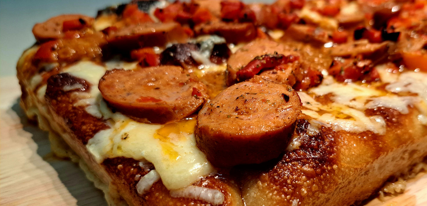 A close-up view of a rectangular Detroit pizza topped with slices of sausage and a rich, chunky sauce. The crust appears thick and golden, indicating a crispy texture.