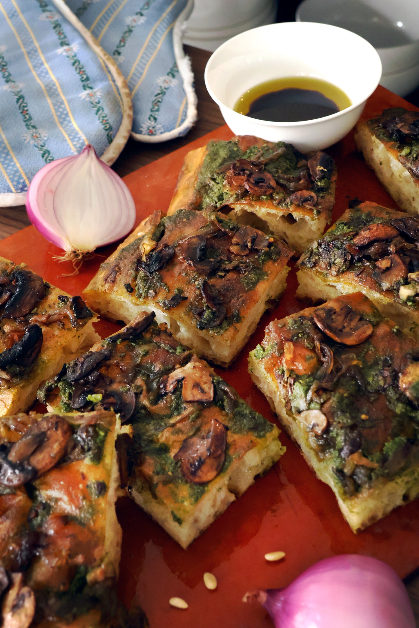 focaccia topped with a vibrant green sauce, likely pesto, and sautéed mushrooms. The bread has a golden-brown crust with a soft, airy interior, visible in the cut pieces.