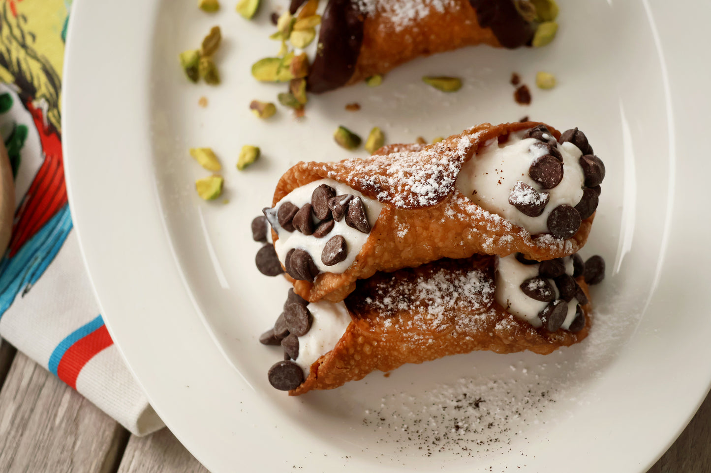 Top view of the chocolate chip cannoli. Cannoli is topped with icing sugar, filled with ricotta with both ends topped with chocolate chips.