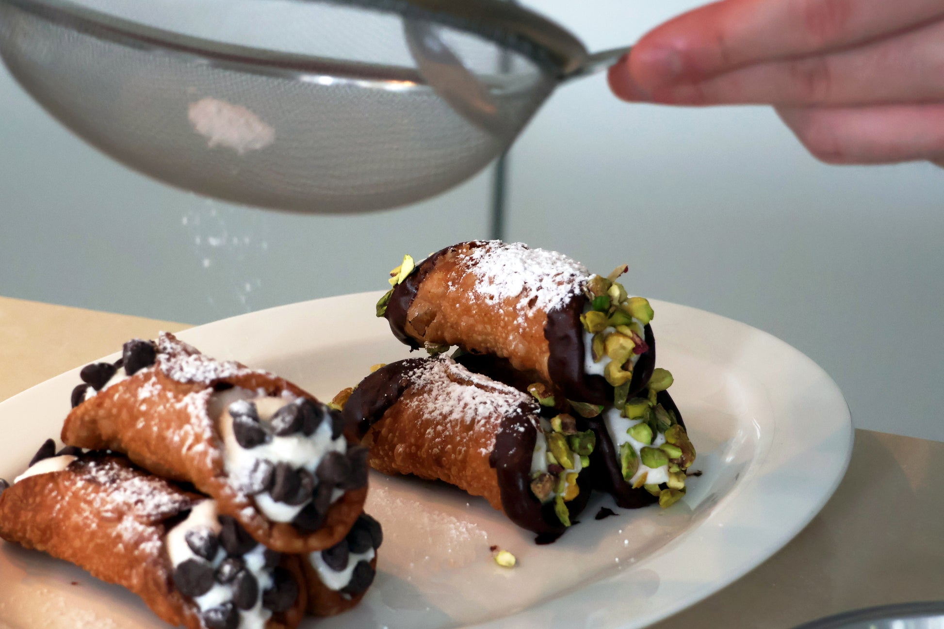 Deep fried cannoli (Chocolate and pistachio flavoured ones) being dusted with icing sugar. 