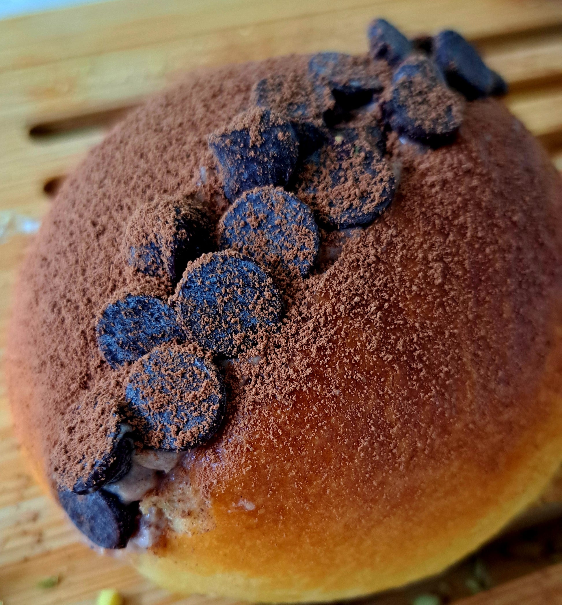 A maritozzo, this time showcasing a chocolate-themed version. The top of the bun is generously covered with a layer of cocoa powder, giving it a rich chocolate flavor. Additionally, there are chocolate chips scattered on top, enhancing the chocolatey appeal.