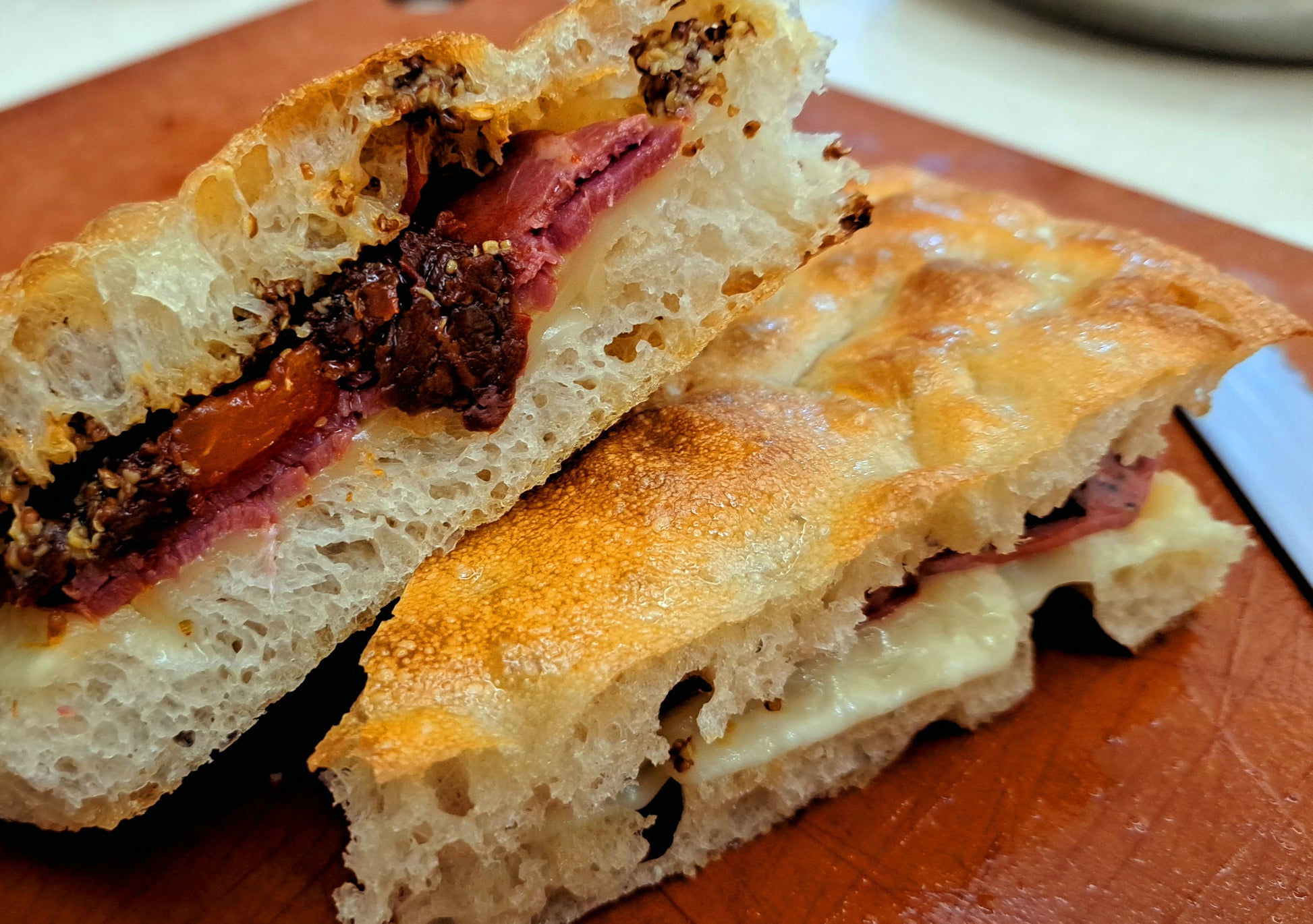 Schiacciata sandwich. Filled with pastrami, melted gouda cheese, sundried tomatoes, whole grain mustard. Toasted till golden brown
